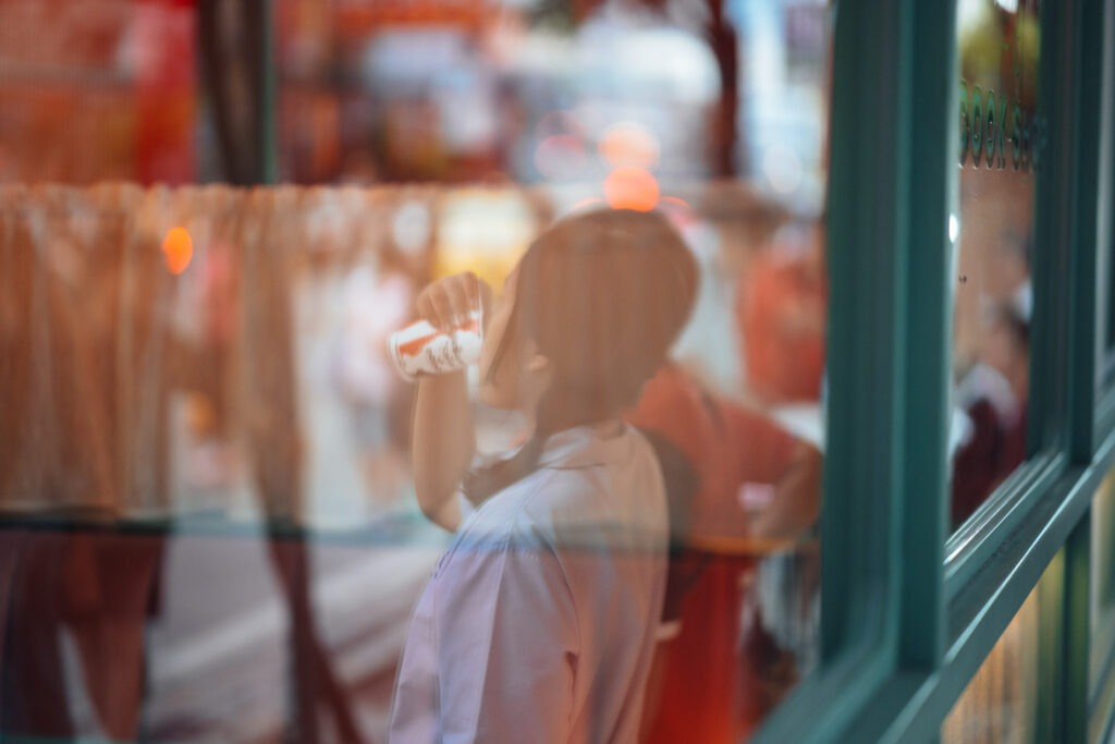 spiegelung in einer scheibe: junge frau trinkt einen kaffe fotografiert mit einer langen brennweite von stefan sperl